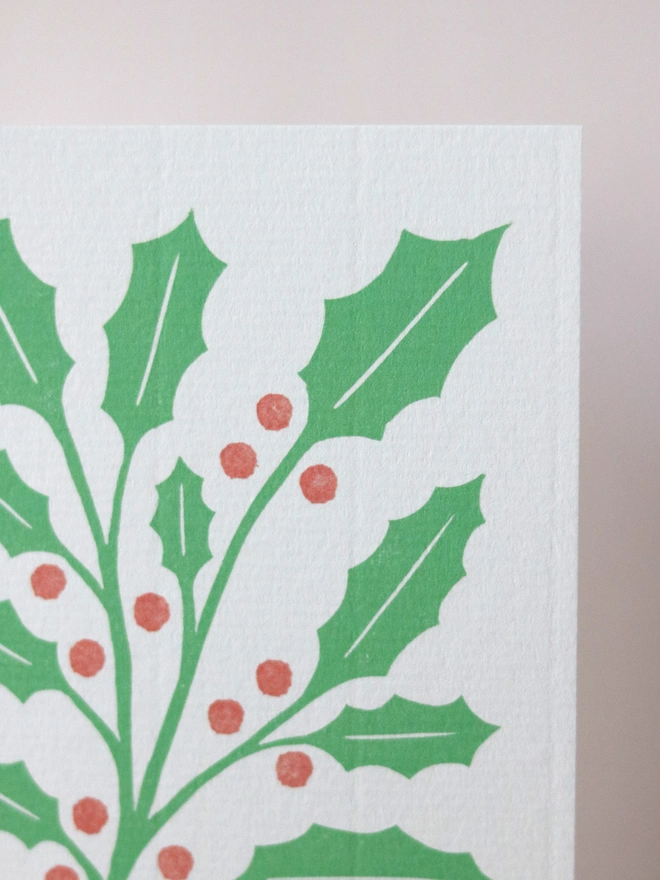 A Christmas card featuring a reproduction of an original linocut print of holly