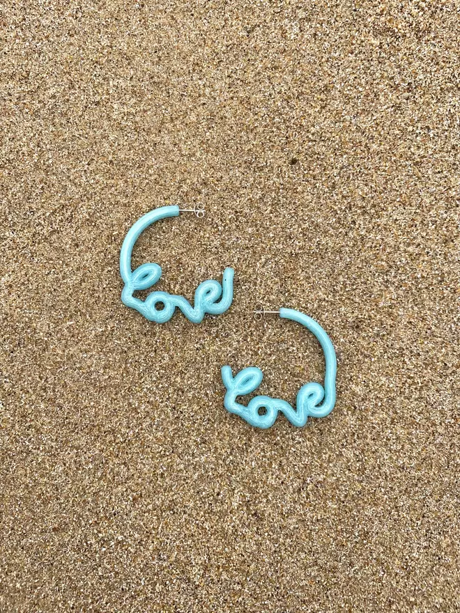 Recycled Ocean Plastic 'Love' Hoops Earrings shot on a sandy beach in the UK 