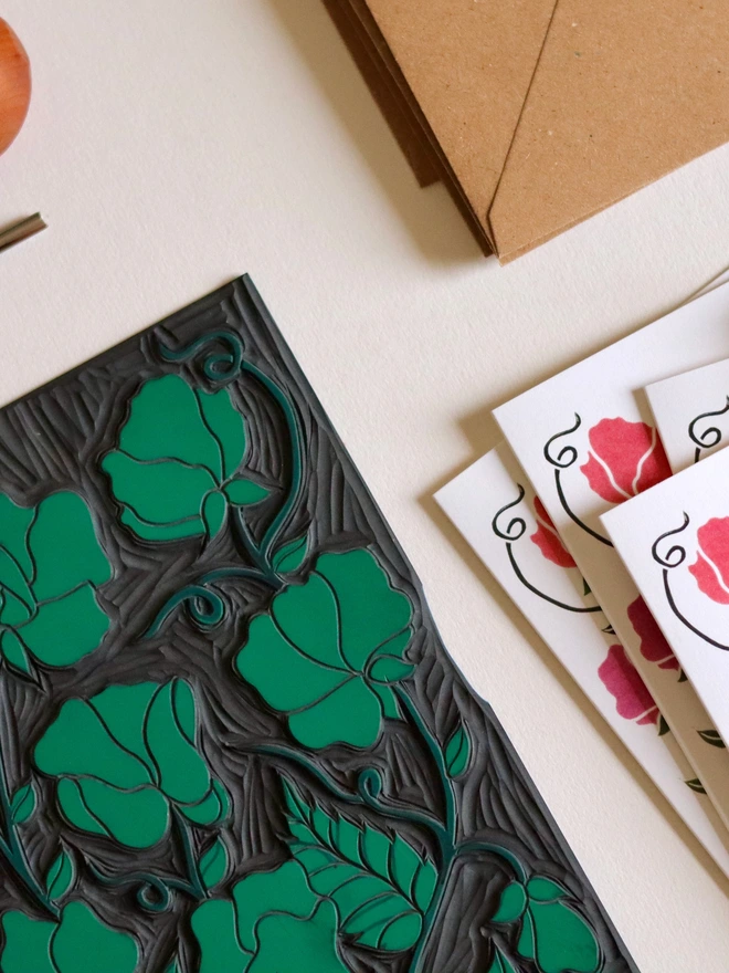 Hand-carved lino block displayed with finished sweet pea flower notecard from set of 8. Traditional relief printmaking block showing carved botanical design. Authentic linocut process, Norfolk countryside studio