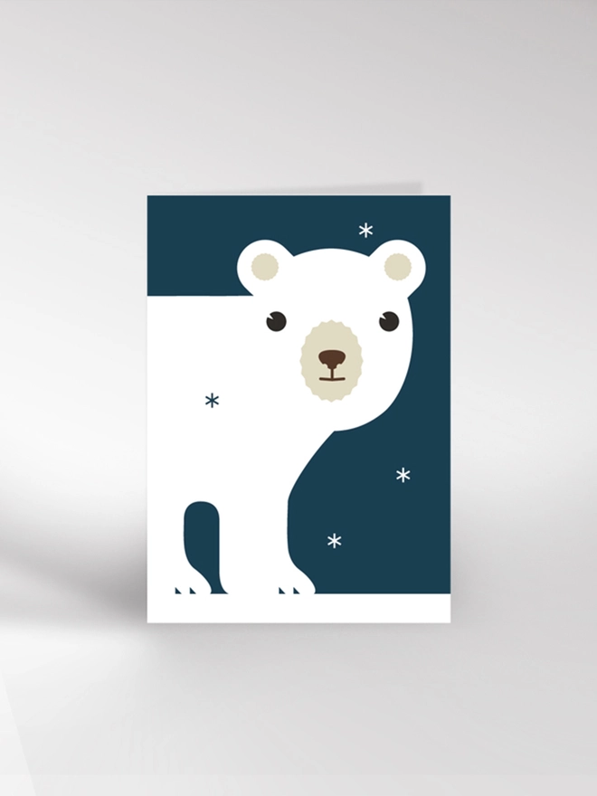 Contemporary illustrated Christmas card featuring a white polar bear on a starry blue background