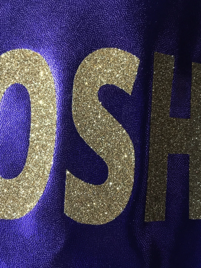 metallic purple fabric with large gold glitter letters