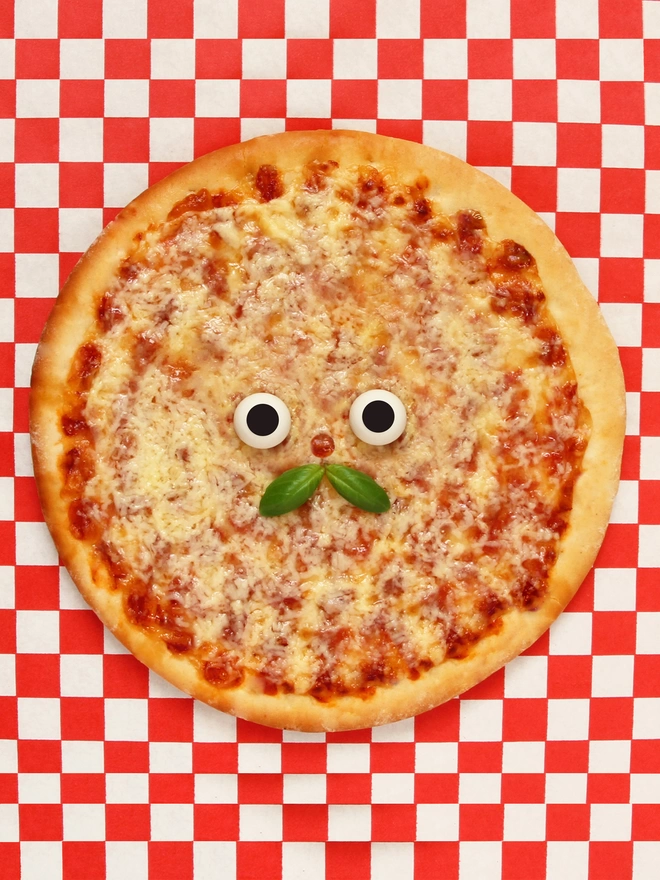 A cheesy pizza card with a basil moustache . On a red and white check tablecloth