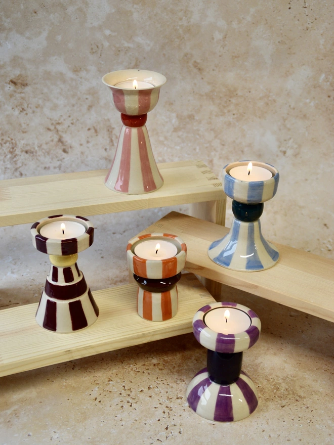 Handmade striped ceramic candlestick holders displayed on a tray, shown in assorted colourways including red, blue and brown