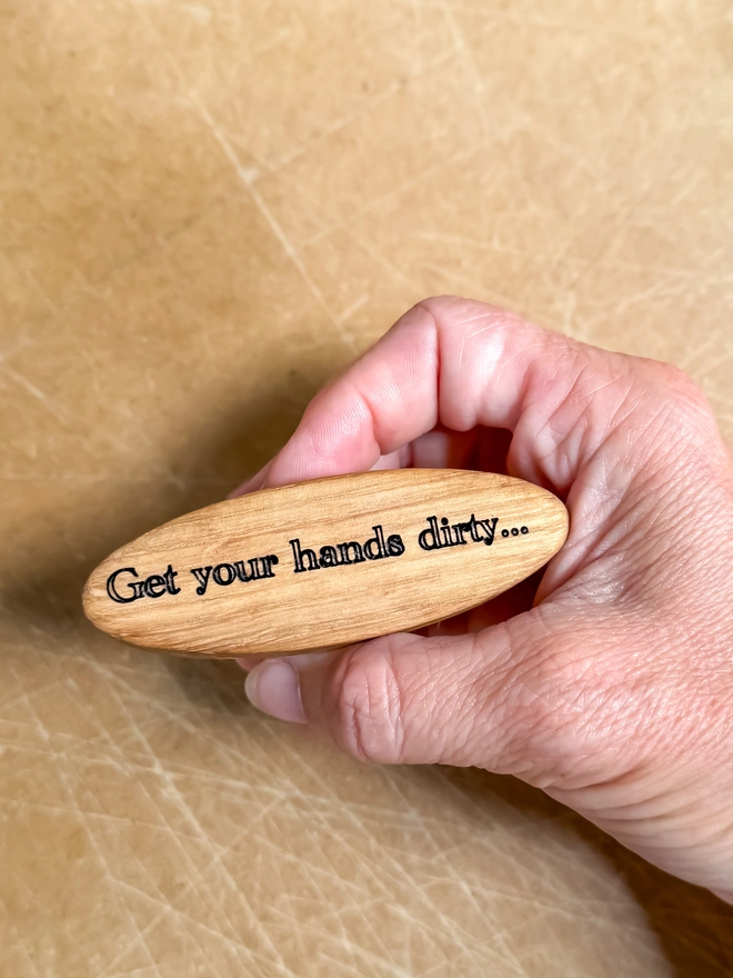 Engraved oak nail brush held in the hand, showing its size in the palm