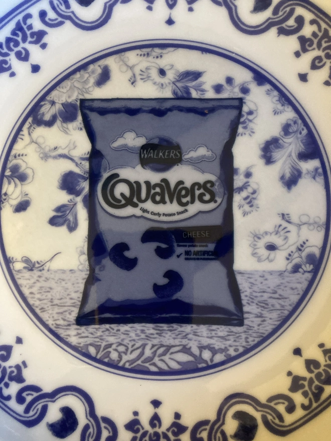 Blue and white Delft style decorative plate featuring a packet of Quavers crisps in the centre.