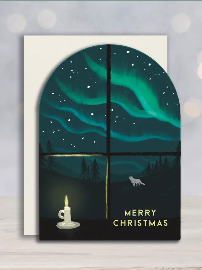 Arched shape Christmas card with white envelope, with an illustrated window snowing the northern lights and a white fox.