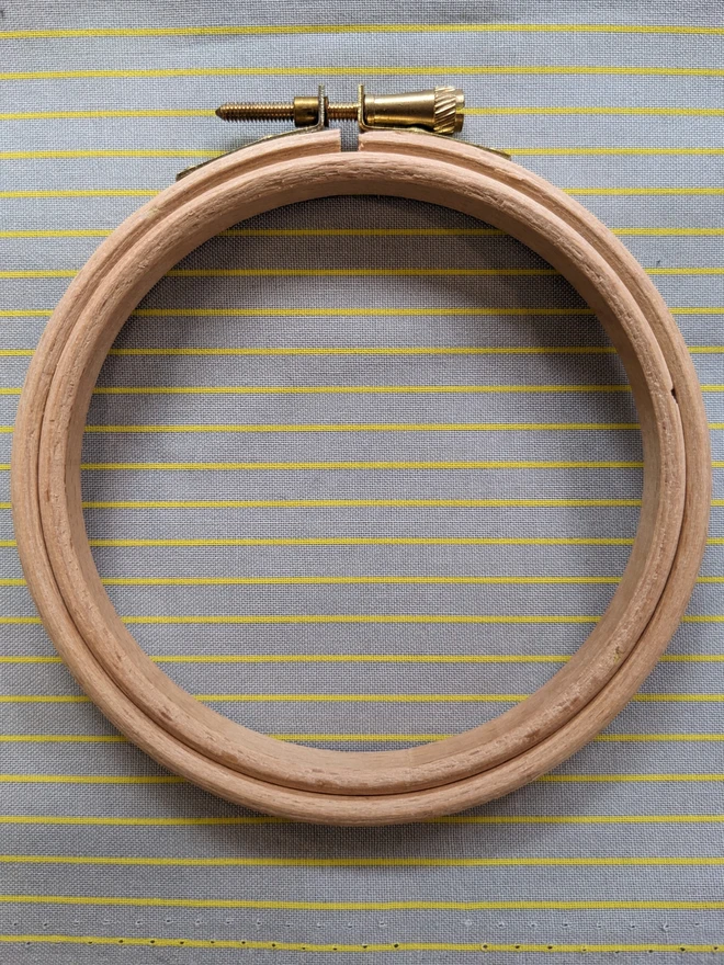 A wooden embroidery hoop lying on a stripy grey fabric