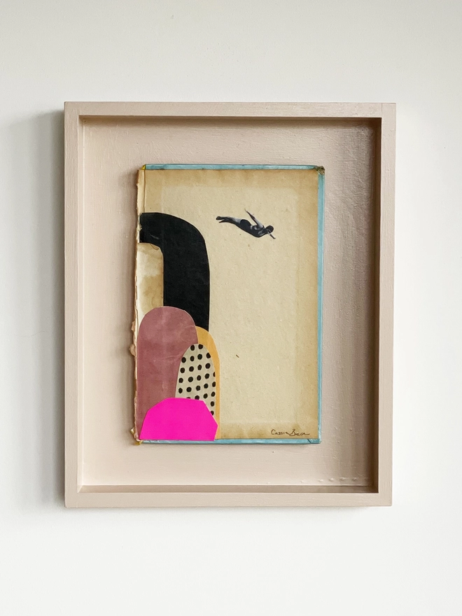 A diving portrait artwork on a vintage book cover, float mounted within a pale pink wood frame.