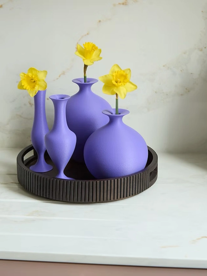 collection of various shaped purple vases with yellow flowers all on a tray