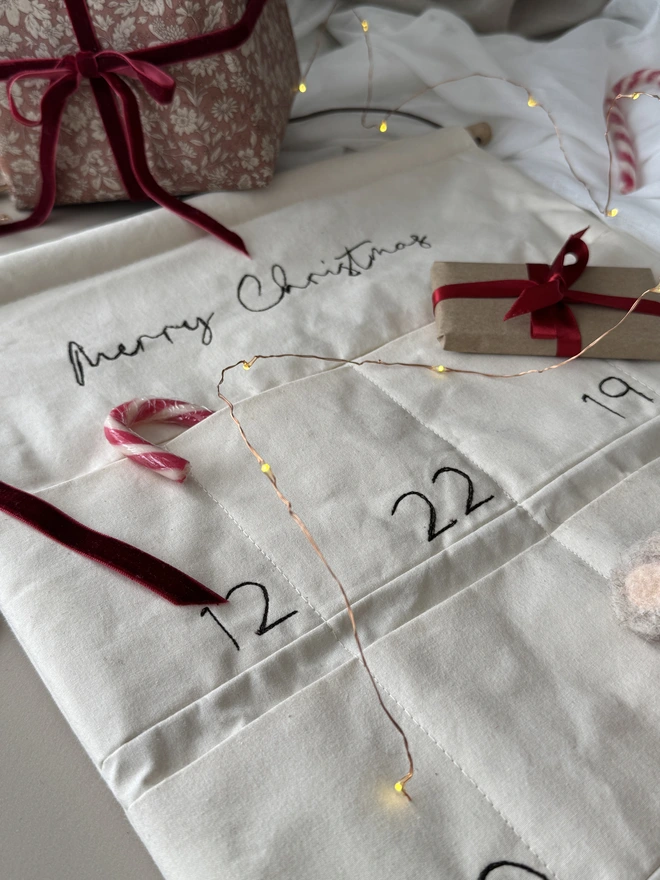 Embroidered Advent Calendar. An Advent Calendar with small gifts and a candy cane lay on top 