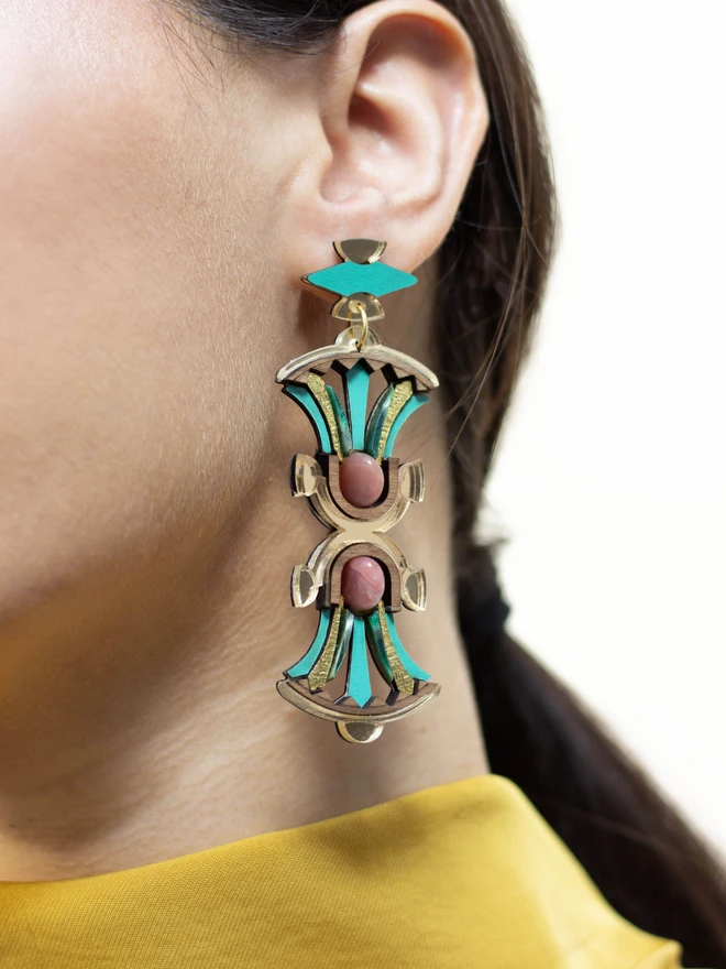 Laser cut earring with gold, green, and pink design on a woman