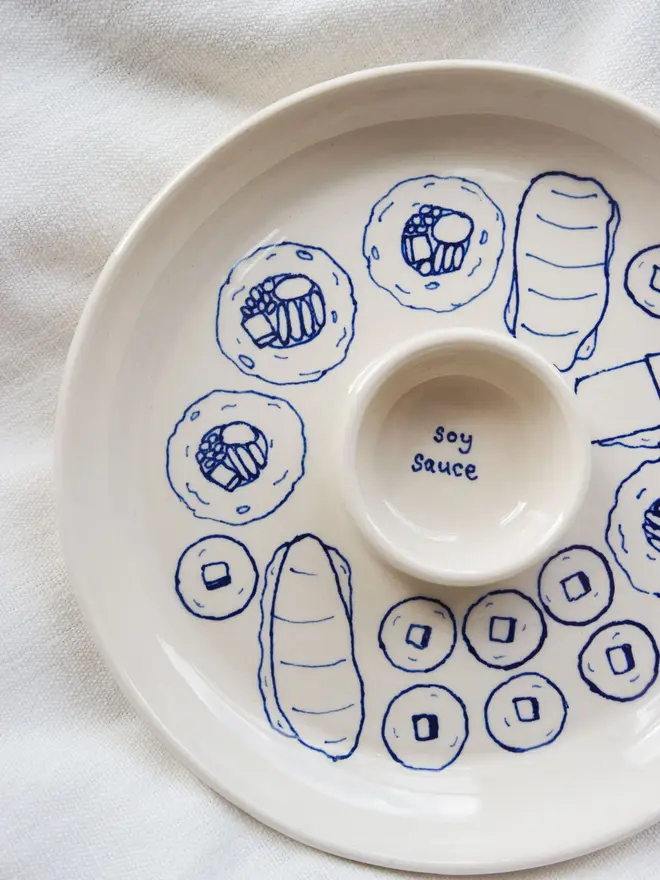 Snack Sushi Dippy Plate, a sushi snack dish sitting on a white surface. The outlines of sushi can be seen in blue. 