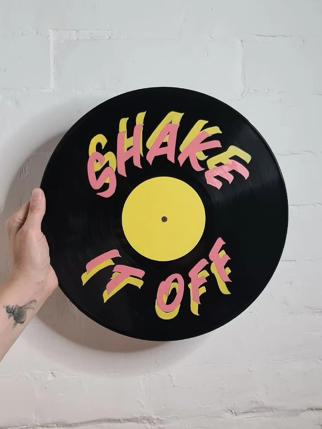 'Shake It Off' 12' Vinyl Artwork, a person holding a colourful vinyl against a stone backdrop 