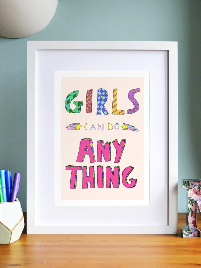 Art print saying 'Girls can do anything' in a white frame in a child's room