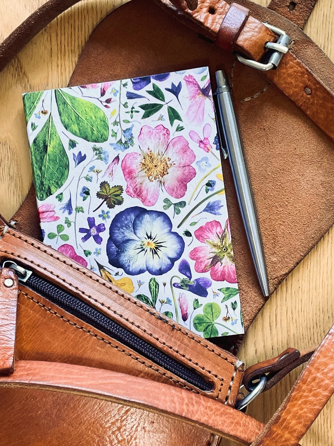 Recycled Pocket Notebook with Delicate Pressed Flower Design on Light Cover and Pen on Wood Table