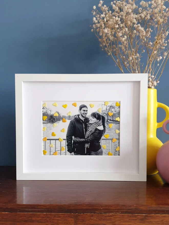 B&W couple photo, with hand embroidered shades of yellow hearts in white frame on desk