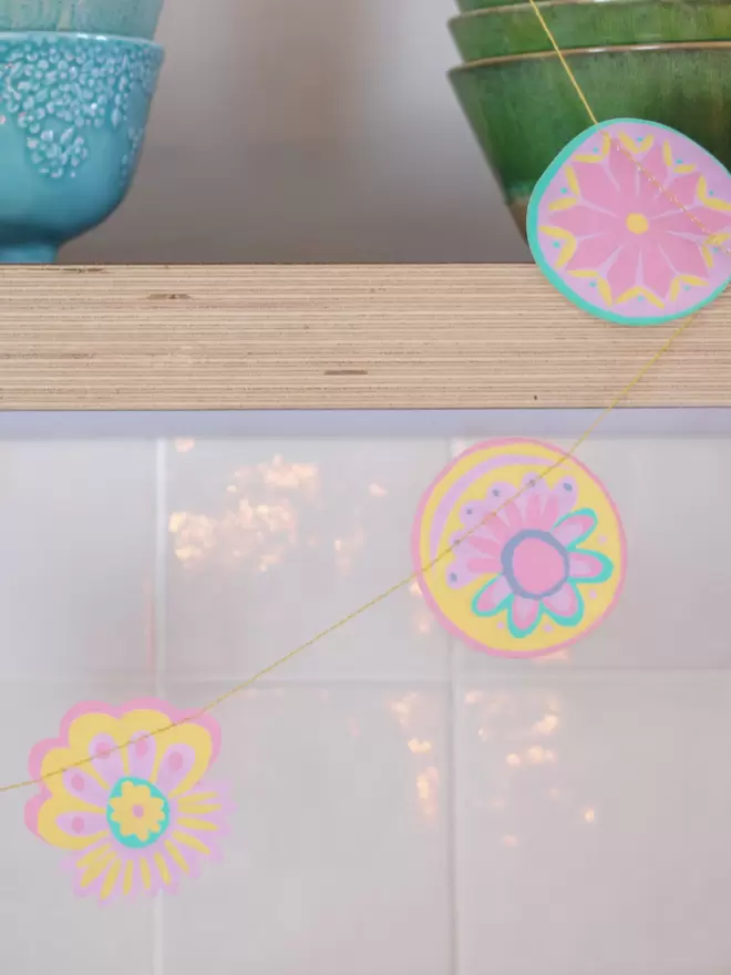 Close up of small pastel shapes, hanging from wooden kitchen shelf