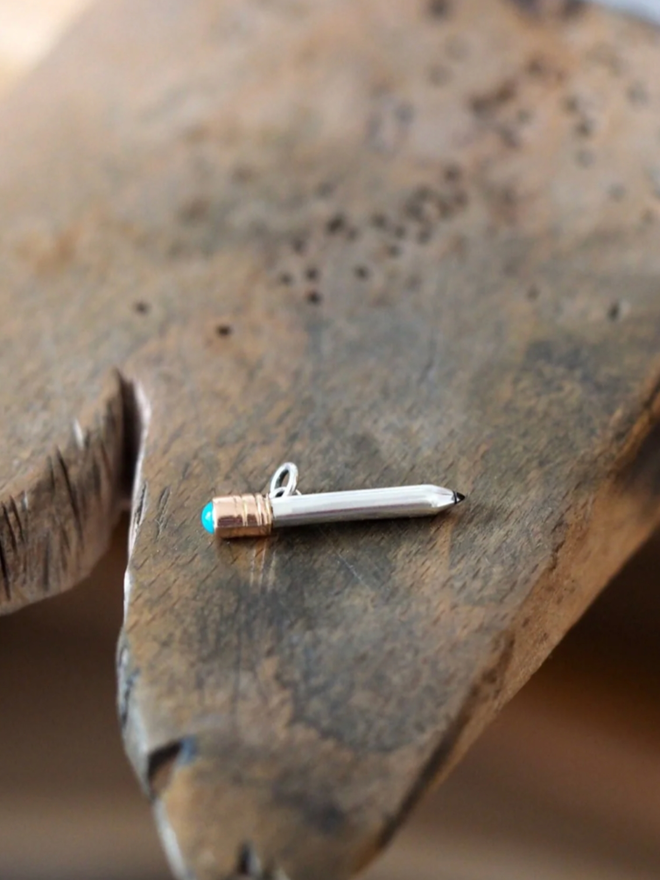 Dinky Pencil Charm. A pencil charm on a piece of wood.