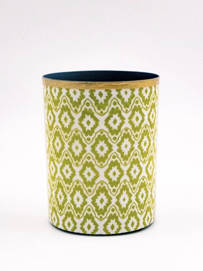 Perfect Enamel Pot. A cylindrical pot covered in lime green and white geometric ikat-style paper with a gilded gold rim and dark interior. The hand-printed design makes a bright desk tidy, plant pot cover or decorative storage piece.
