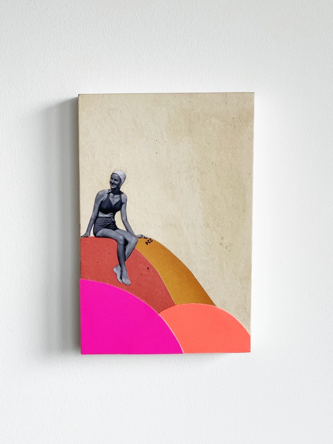 A brightly coloured artwork made with a mix of neon pink and orange card and vintage papers. It is a female portrait of a swimmer who is about to dive off the colourful rocks into the sea.