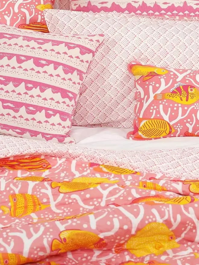Pink Coral Reef Quilt, a pink quilt sitting on a bed. It is accompanied by some pillows. 
