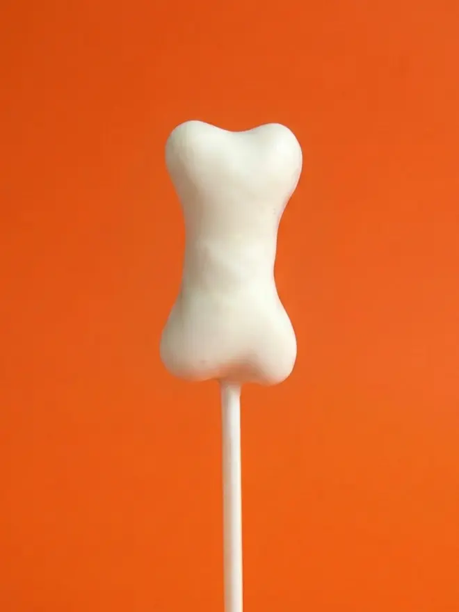 Halloween bone cake pop on a white stick against a bright orange background
