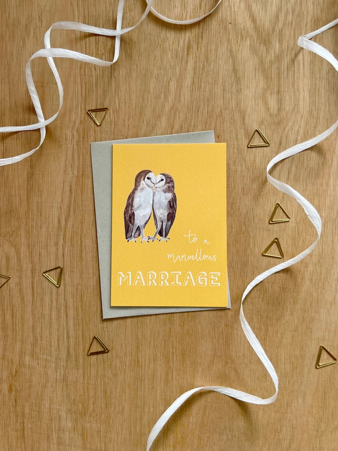 a greetings card with a bright yellow background featuring two kissing barn owls and the phrase ‘to a marvellous MARRIAGE”