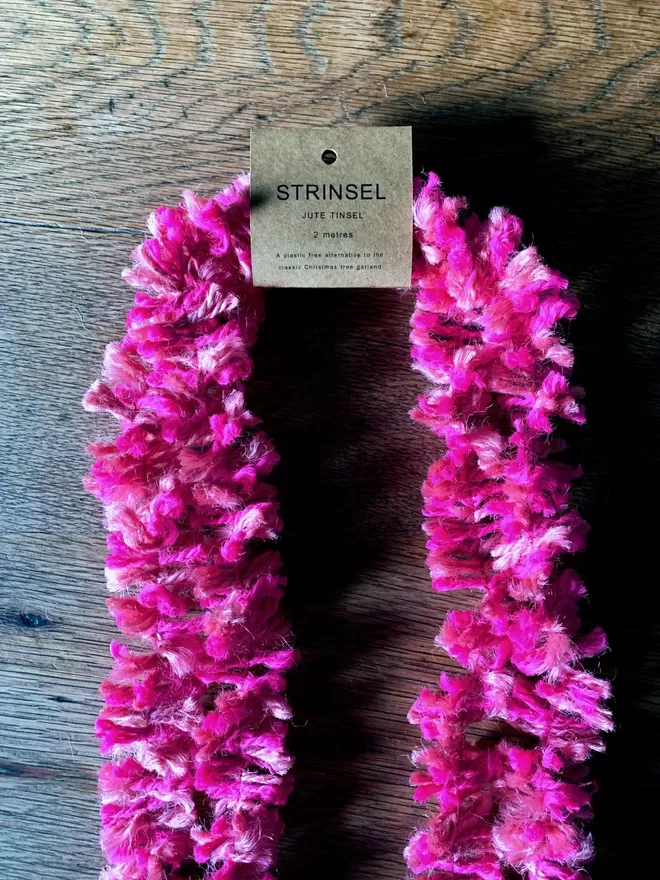 Bright pink jute string tinsel AKA Strinsel packaged in a kraft card label on an oak table