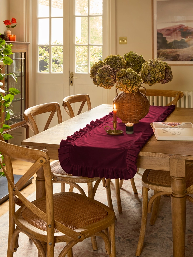 Handmade burgundy velvet ruffled table runner on oak dining table styled with hydrangeas and candles, Kika Bespoke
