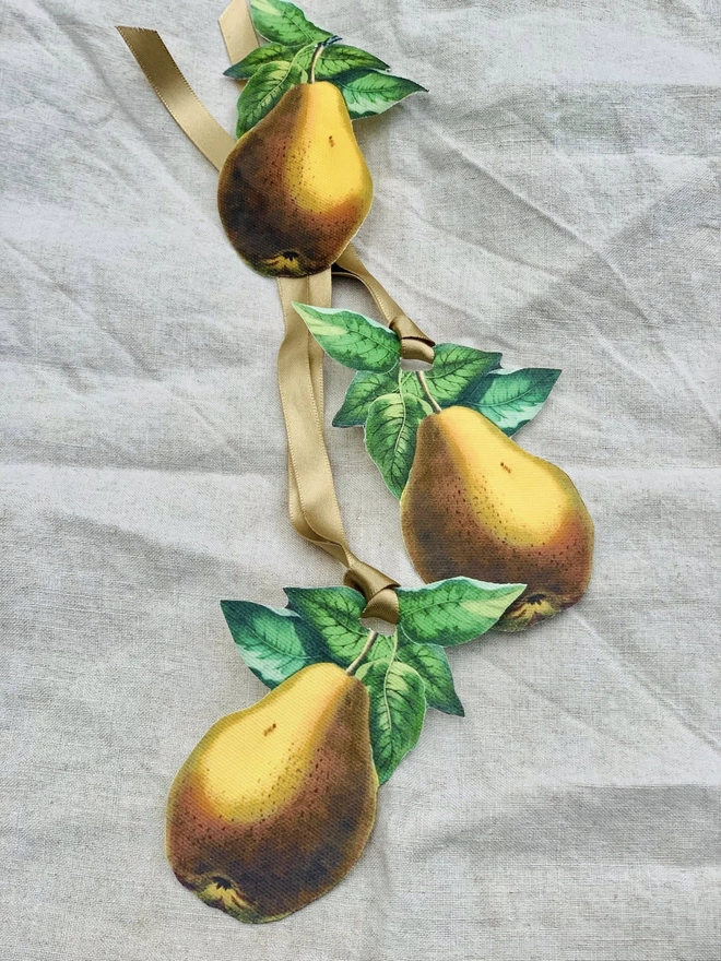 Three golden pear table decorations for tying around napkins, on an unbleached linen tablecloth