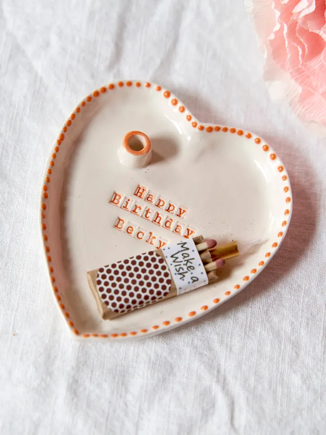 Personalised ceramic heart birthday dish with a candle holder with an orange dotted rim design, placed on a plain white tablecloth 