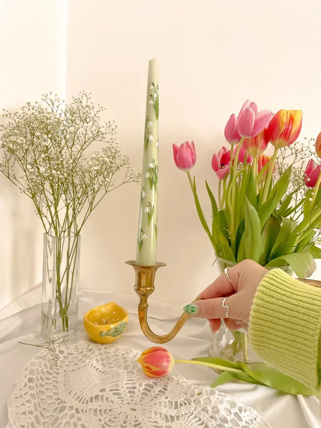 Snow Drops Handpainted Candle, a green snowdrop candle standing on a table accompanied by flowers