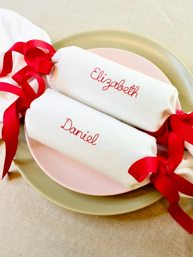 White cotton fabric Christmas cracker napkins personalised with names and red grosgrain ribbon bows
