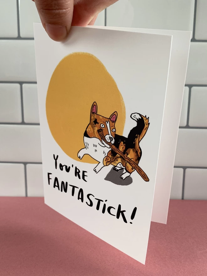 A6 greeting card that reads - You're Fantastick! Illustrated with a corgi dog with a stick in its mouth