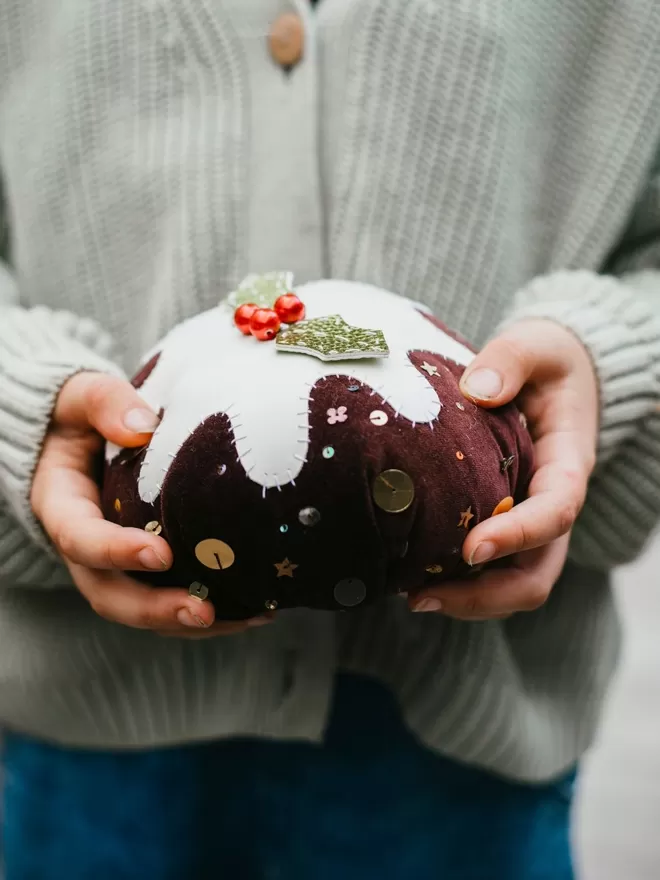 Christmas Pudding seen held by someone wearing a green jumper.