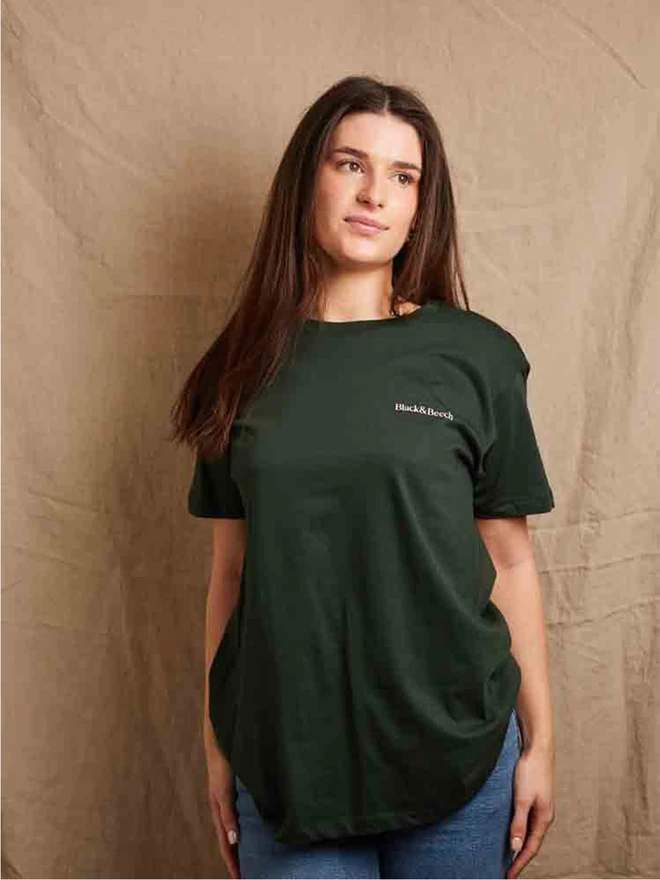 Model is showing the front of the forest green feminist icon t-shirt. Our companies name - Black & Beech is printed in pale pink on the left chest 