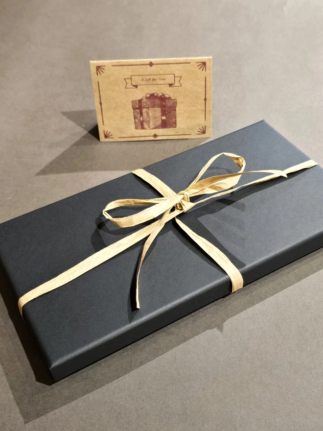 a black gift box with a Kraft colour ribbon containing a leather escape map pen case