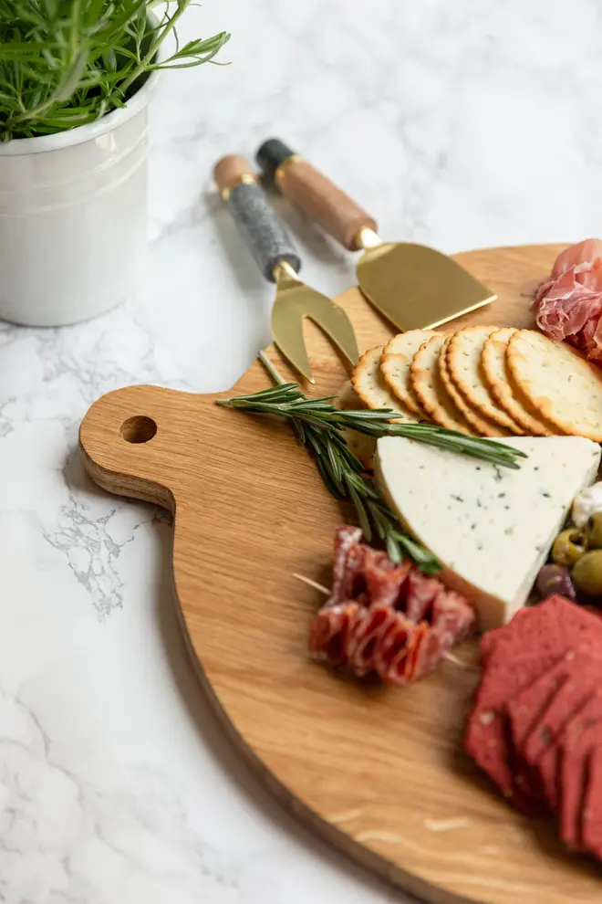 Large Oak Oval Serving Board, a wooden serving board sat on a stone surface accompanied by a spread of food. 