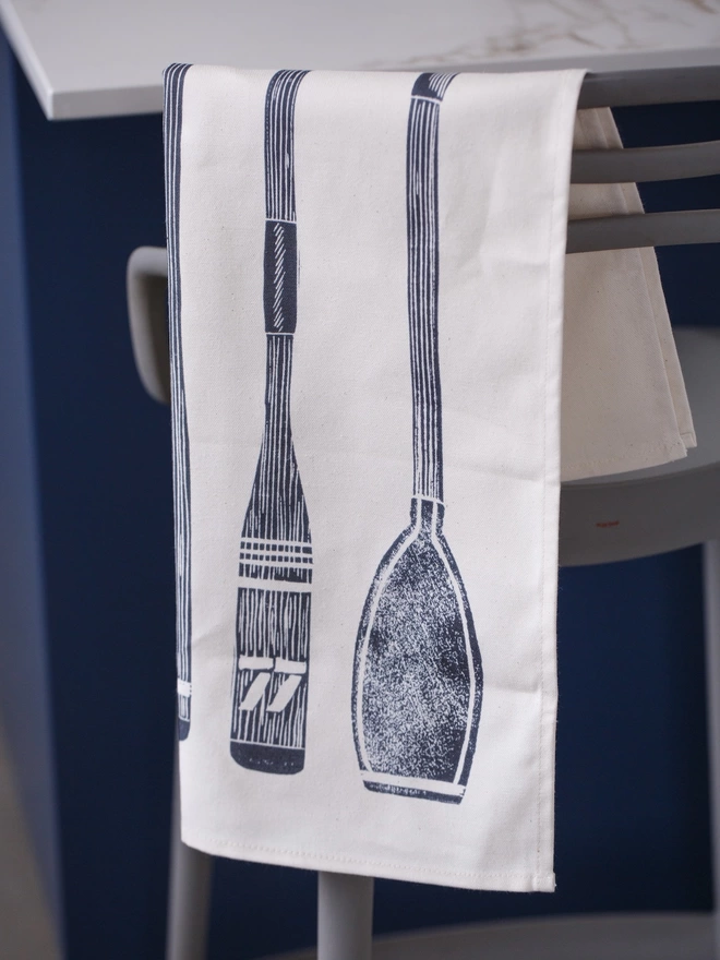 Picture of a tea towel on a chair with an image of oars and paddles, taken from an original lino print
