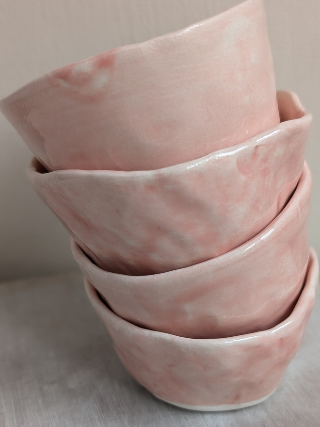 a stack of pink ceramic hand made small pots on a wooden surface