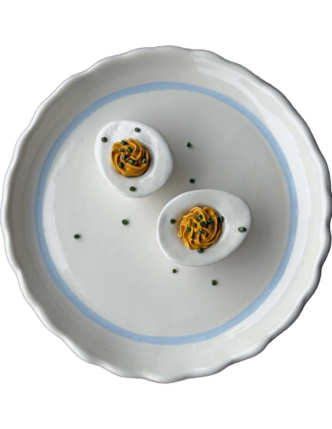 Ceramic devilled eggs with chive detail, on a plain white plate with blue trim, with a cut out background