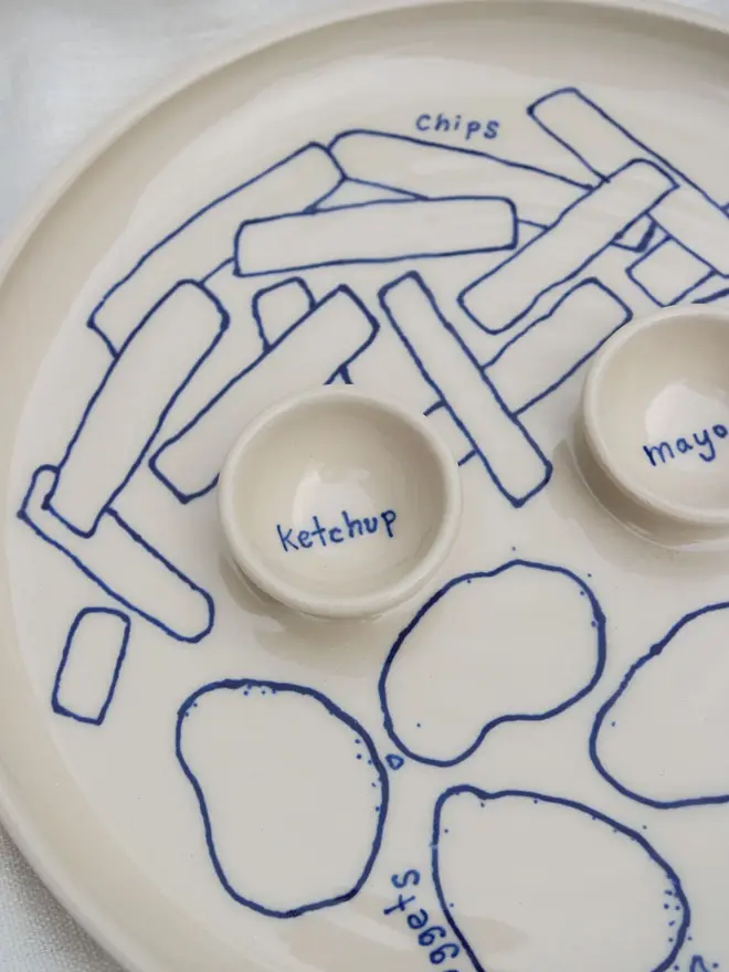 Dippy Chips & Nuggets Dinner Plate, a white dip dinner plate with blue outlines for nuggets and chips sitting on a white bed cloth. 