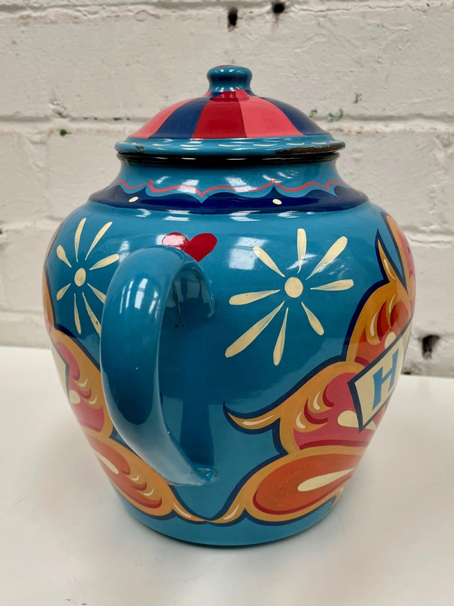 Large blue vintage enamel teapot, hand-painted with a traditional fairground inspired design in pink, yellow and orange. 'Hope' is painted in a banner across the centre.