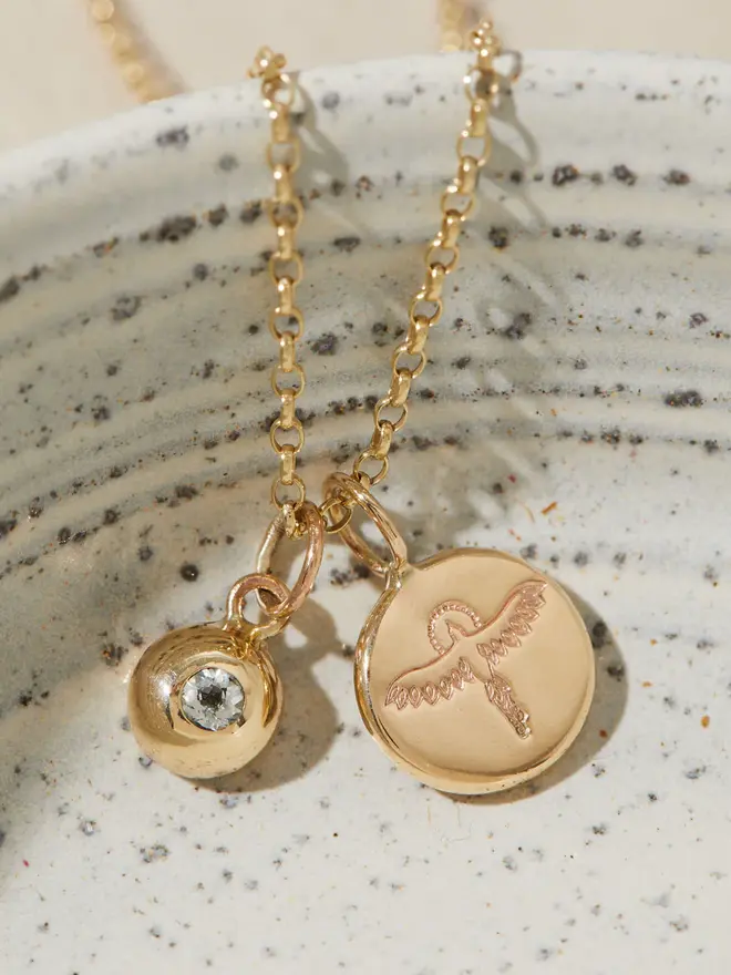 9ct Gold Phoenix Pebble Necklace with a birthstone charm hanging over a bowl