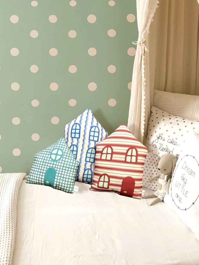 Set of 3 house cushions lying on a child's bed with other cushions and a dotted wall
