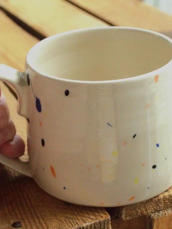 Large creamy white terrazzo cups with black, blue, and yellow splatters and glossy glaze on a wooden surface.