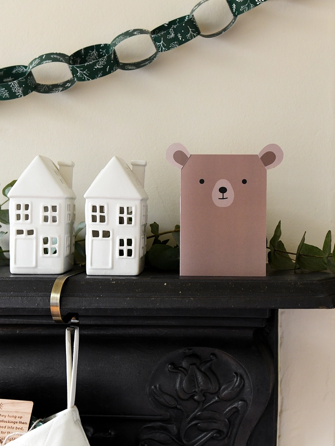 A brown bear greetings card stand on a black mantlepiece where two patchwork stockings are hanging from.