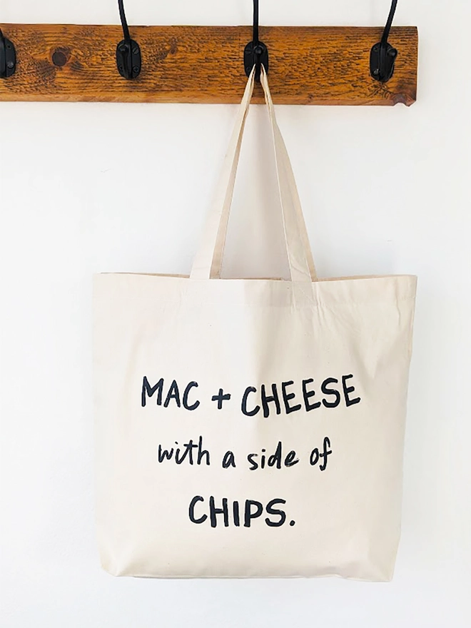 A natural coloured canvas tote with black slogan reading Mac and Cheese with a side of Chips