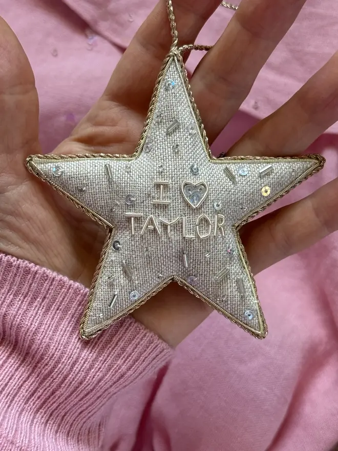embroidered linen 'i love taylor' star decoration. embroidered star hanging ornament photographed on pink background.