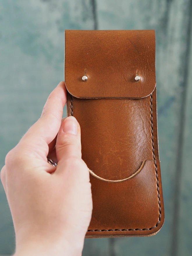 A hand holds a small slim leather darts sleeve.